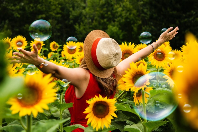 Anbieter tanzend im Sonnenblumenfeld umringt von Seifenblasen. act Ideen.