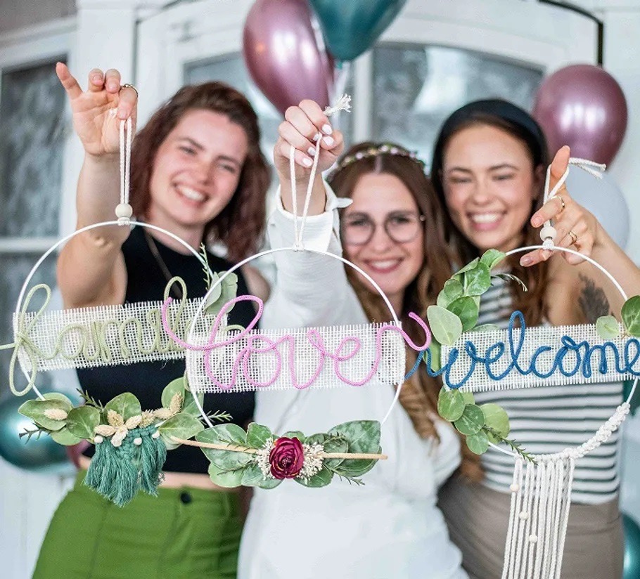 Drei lachende Frauen zeigen ihre unterschiedlich gestalteten Ringe mit Schriftzügen, Blüten und Makramee