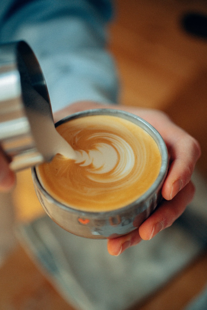 Eine Person gießt ein feines Muster in eine Tasse Kaffee