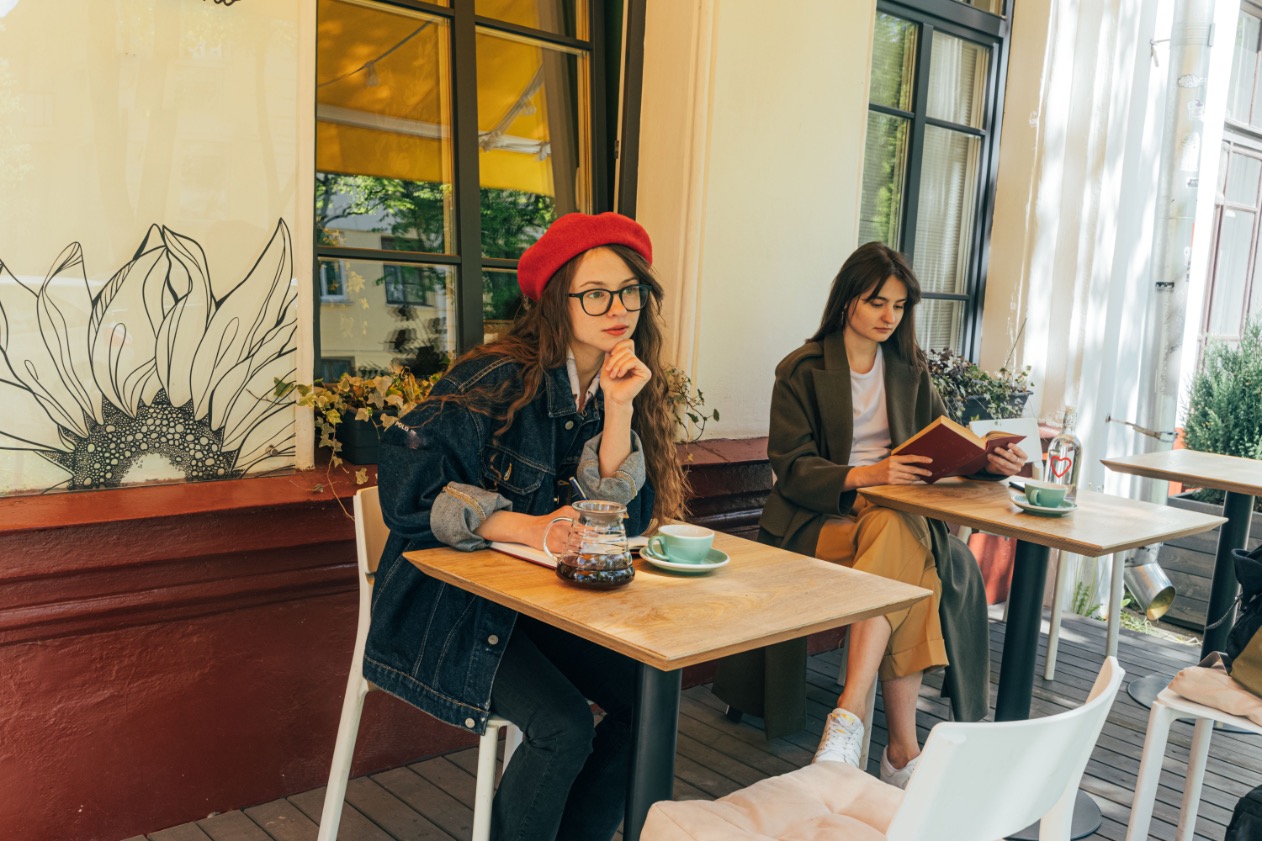 Two people sitting with coffee and a notebook at tables in a bright café