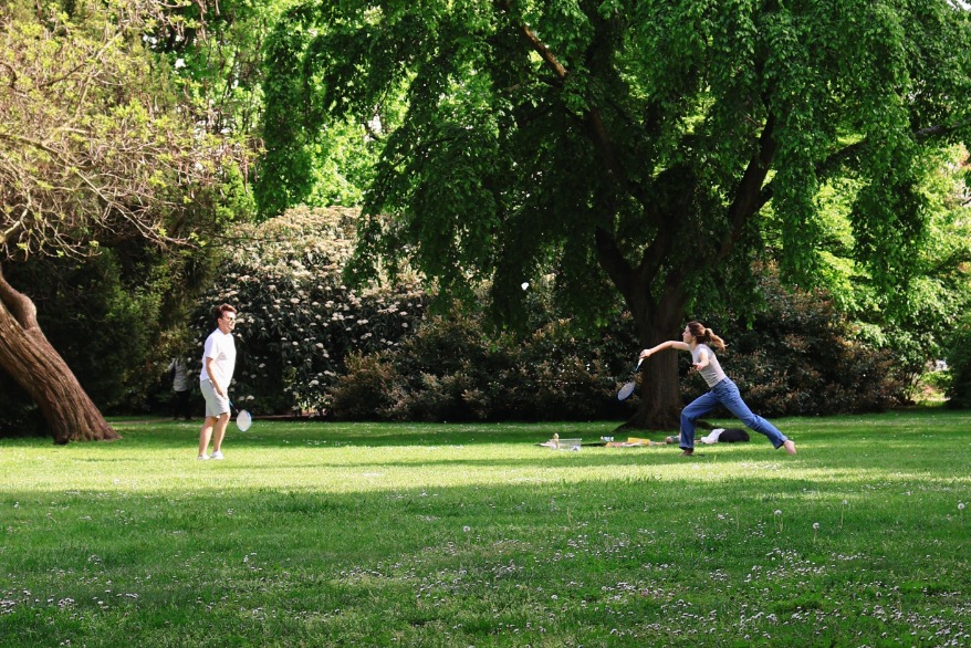 Two people playing badminton together in a green park