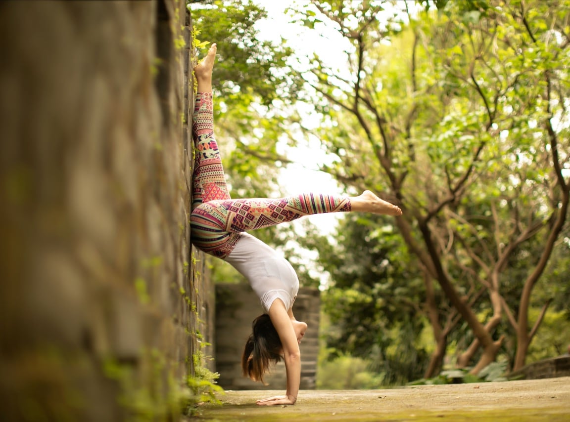 Eine Frau übt bei einem Outdoor-Yoga-Moment einen Handstand im Grünen